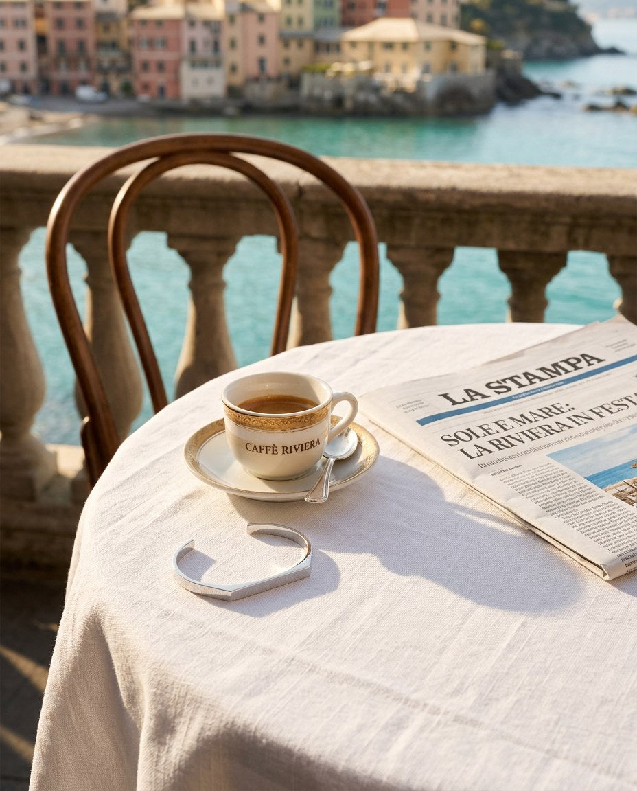 The Aura Signet Bracelet sobre una mesa de café junto al mar con espresso